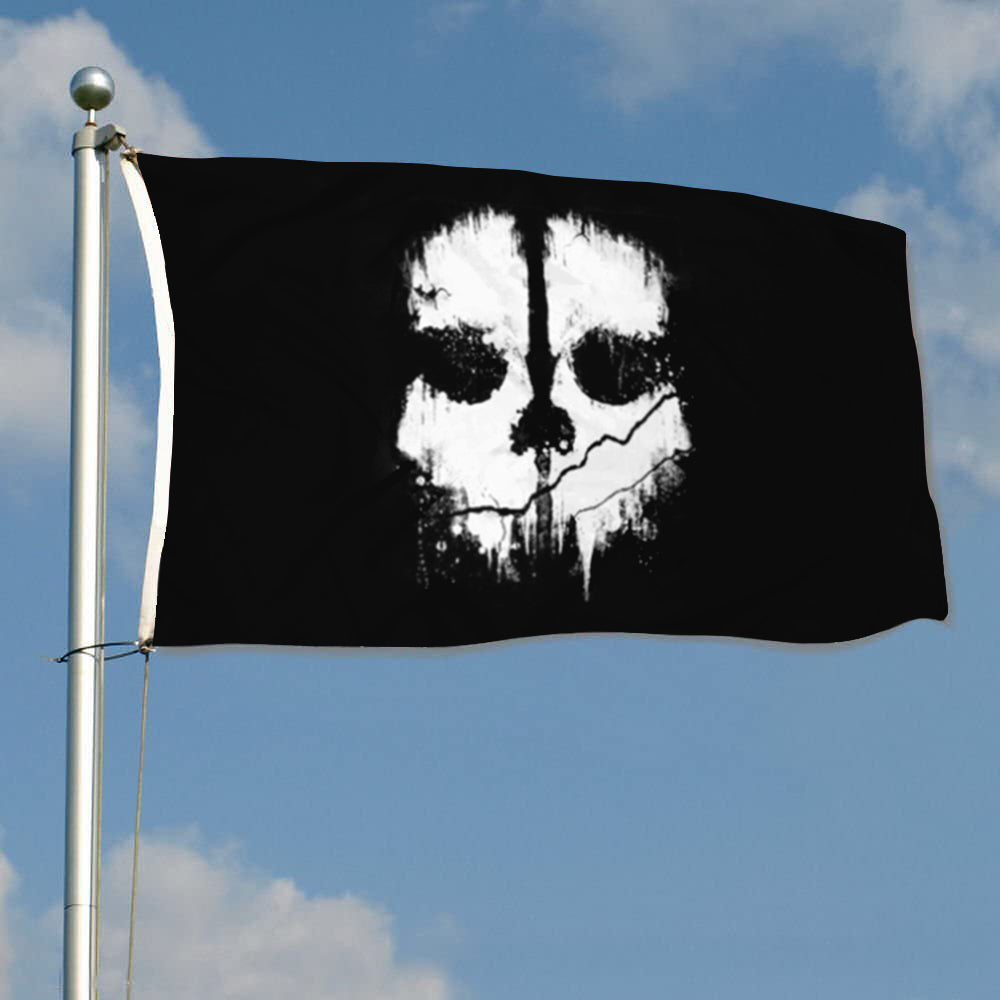 Black flag with white stylized skull face design waving on flagpole against blue sky.