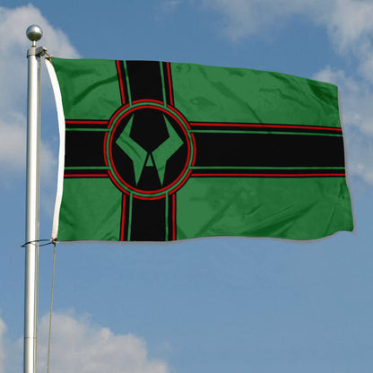 Green Latveria flag with black and red cross and circular emblem on a pole against blue sky.