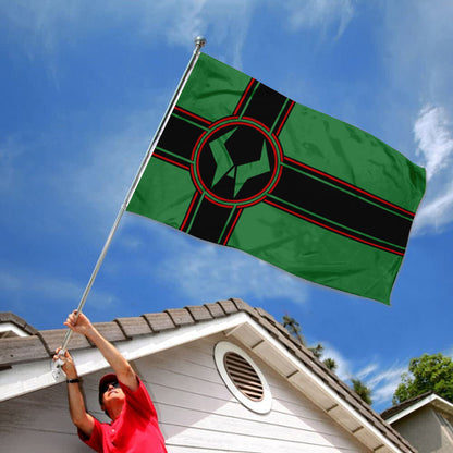 Latveria flag with green background and black and red cross design flying on pole against blue sky.